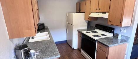 Una cocina compacta con gabinetes de madera, un refrigerador blanco, una estufa y un microondas.