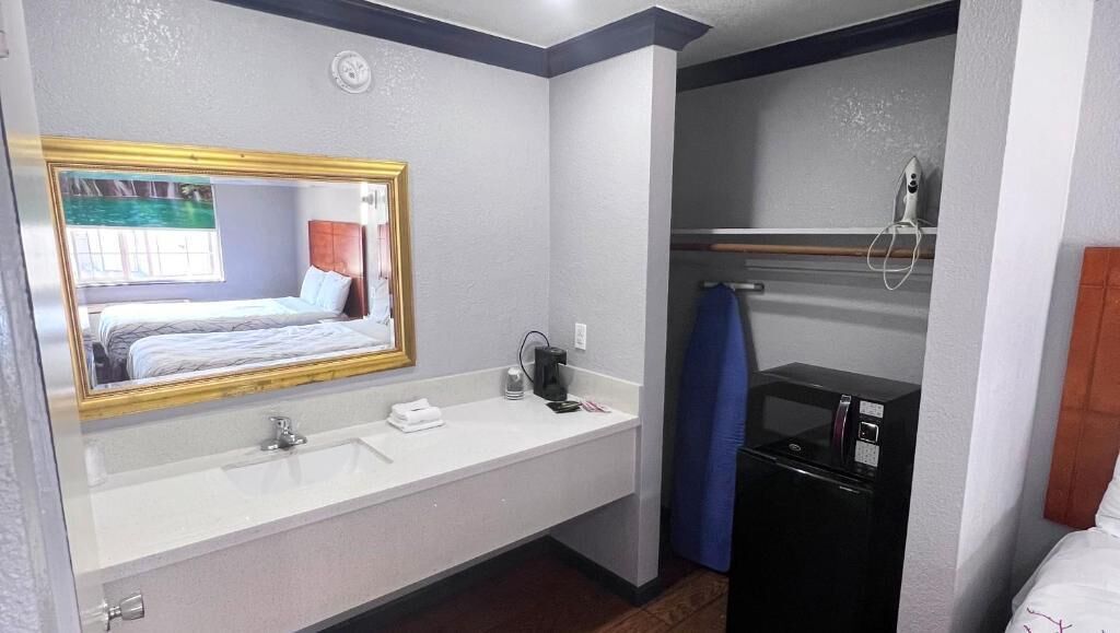 Ein Hotelbad mit einem großen Spiegel, einem Waschbecken, einer Dusche und einem Bett.