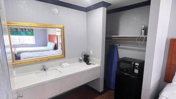 A hotel bathroom with a large mirror, a sink, a shower, and a bed.