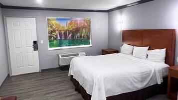A bedroom with a large bed, a window with a nature scene, a white door, and a small bedside table.
