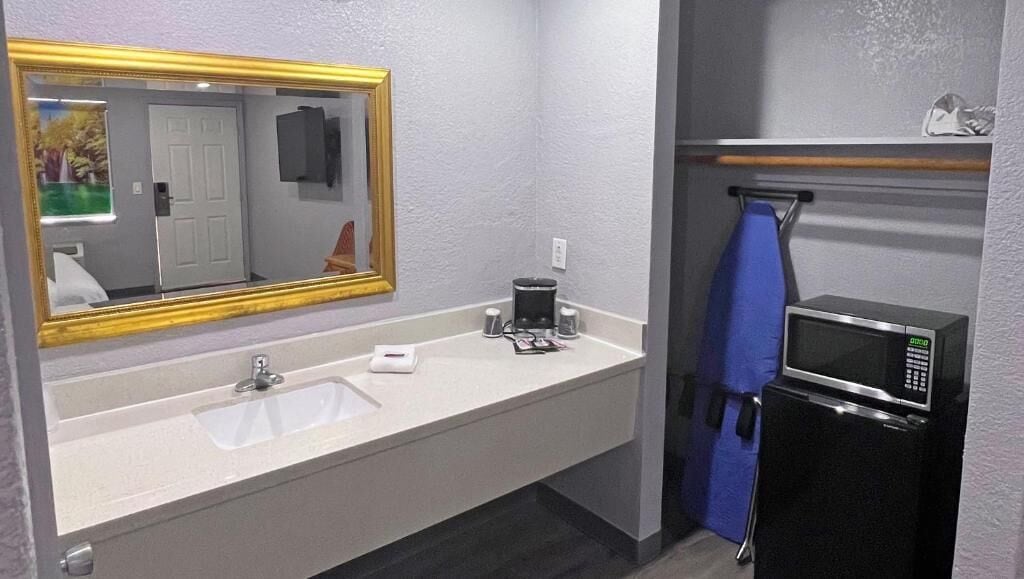 A bathroom with a sink, mirror, towel rack, and a microwave.