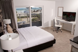 Habitación de hotel con cama, escritorio con computadora, televisor y balcón con vista a la playa.