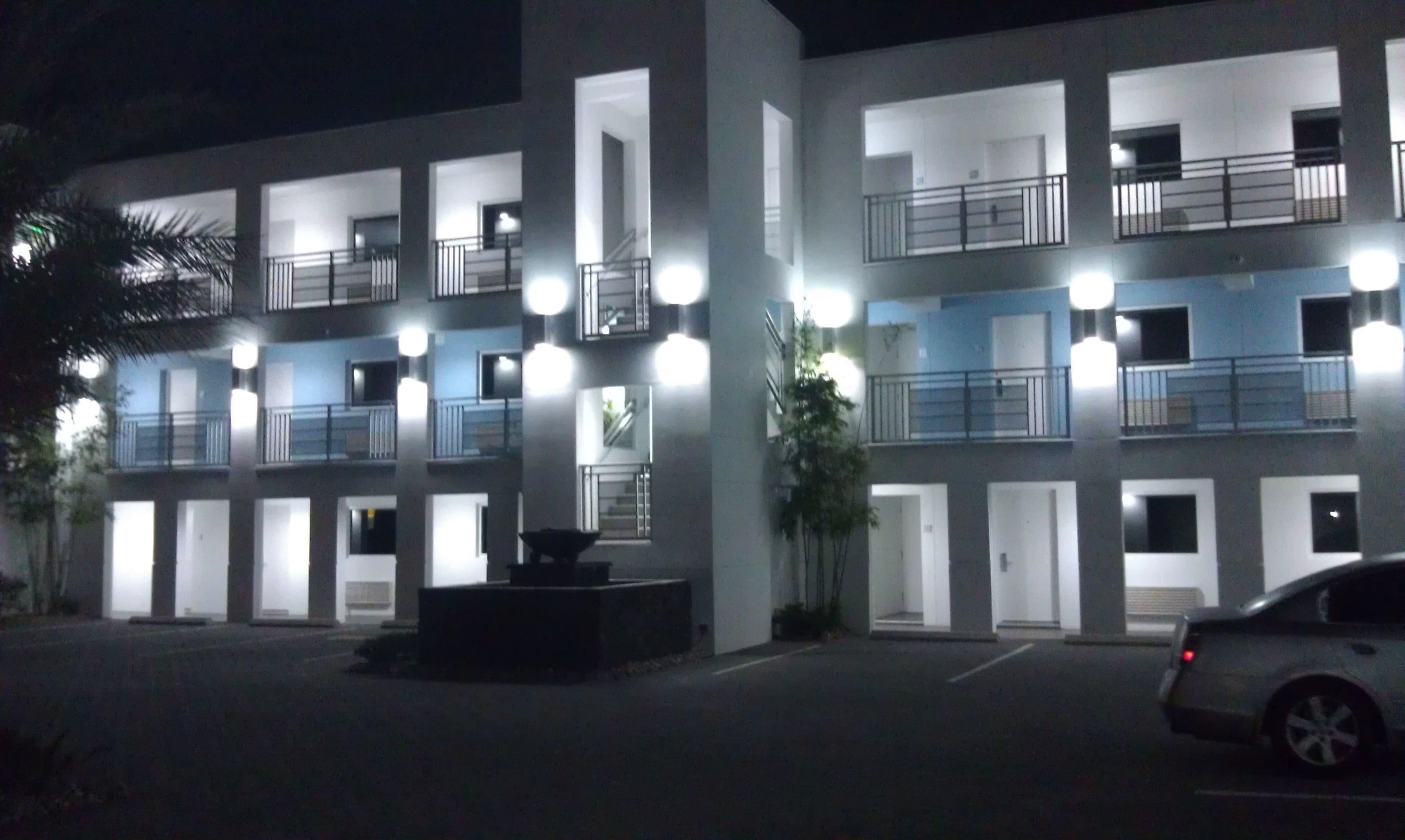 A multi-story hotel with balconies, a parking area, and a central courtyard.
