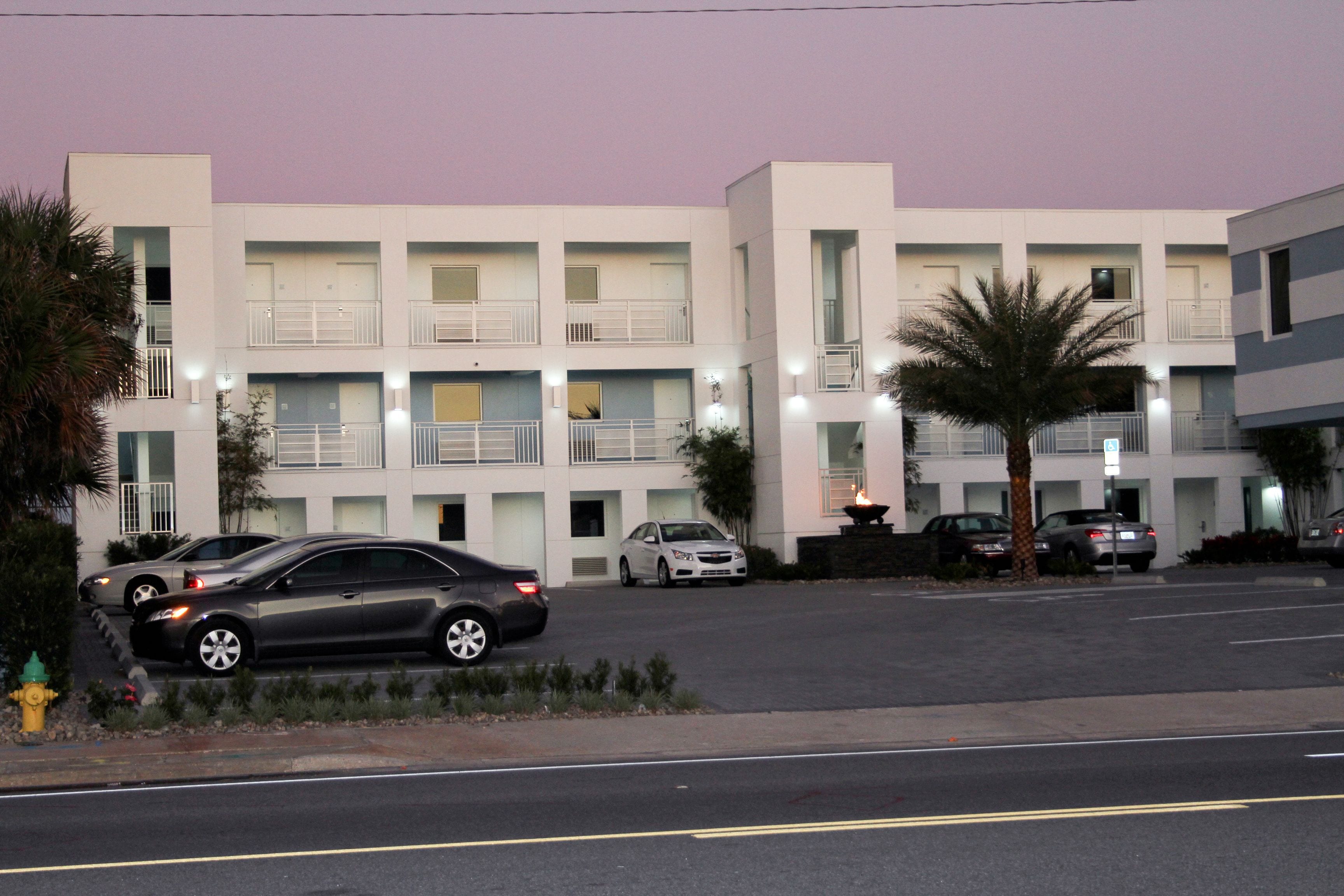 A multi-story hotel with balconies, a parking lot, and a palm tree.