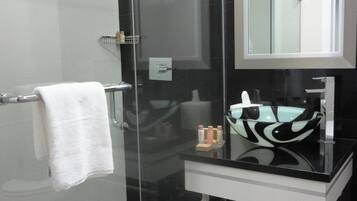 A modern bathroom with a glass-enclosed shower, a black sink with a glass bowl, and a large mirror above the sink.