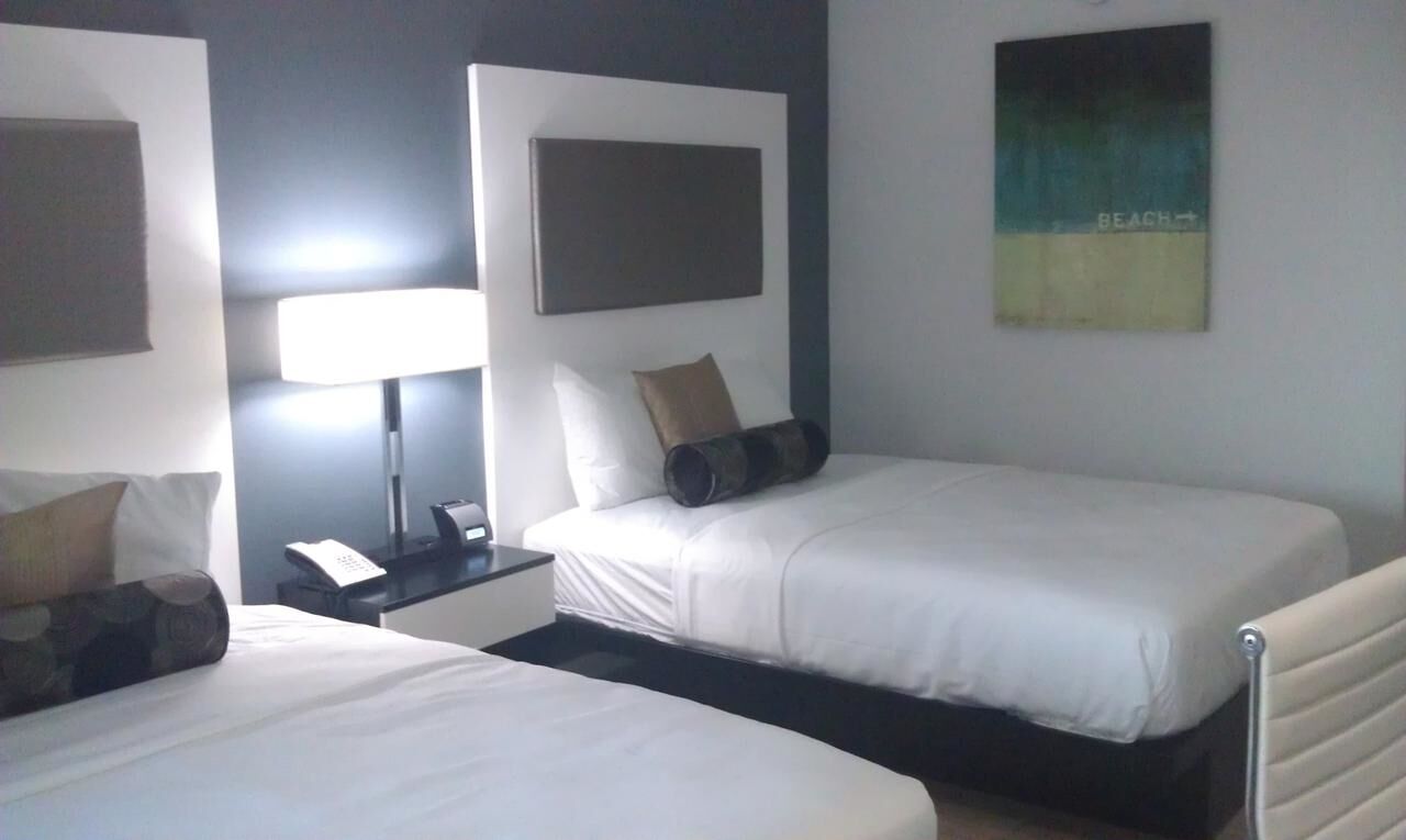 A hotel room with two single beds, a bedside table with a lamp, a phone, and a wall-mounted artwork.