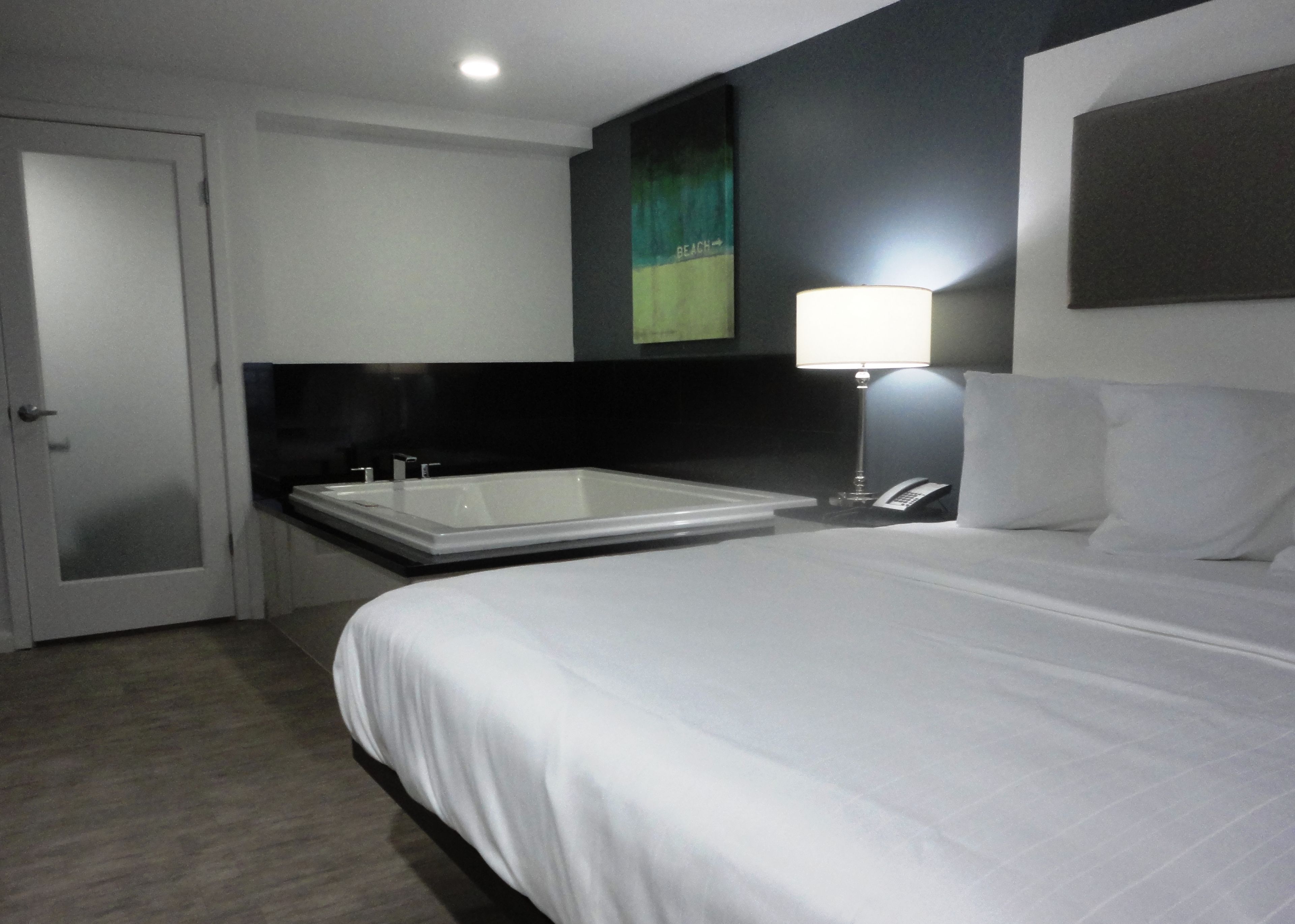 Une chambre d’hôtel moderne avec un grand lit, une baignoire séparée, une lampe de chevet et un téléphone sur la table de chevet.