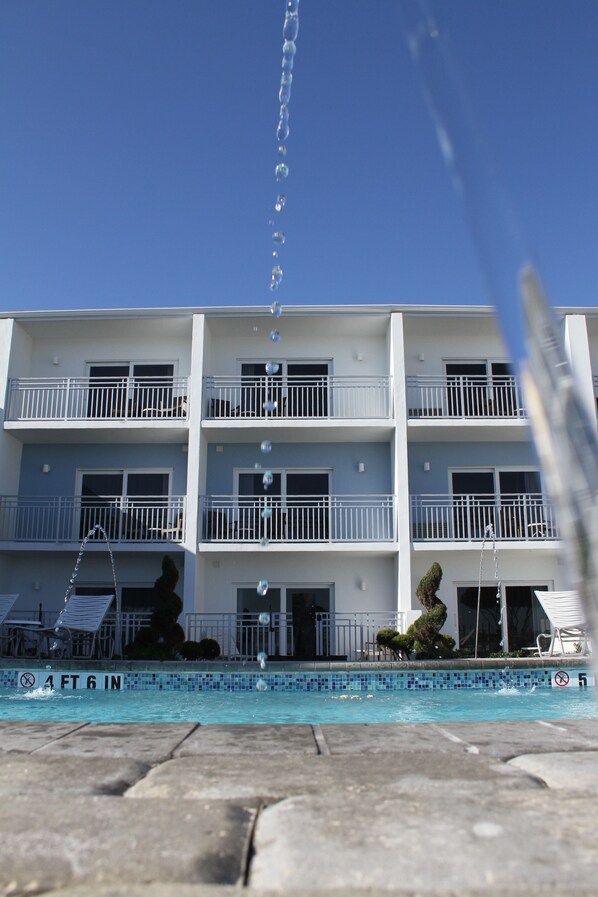 A multi-story hotel with balconies, a swimming pool, and a clear blue sky.