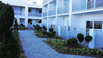 Un hotel de varios pisos con fachada azul y blanca, un sendero pavimentado y setos recortados a lo largo del camino.