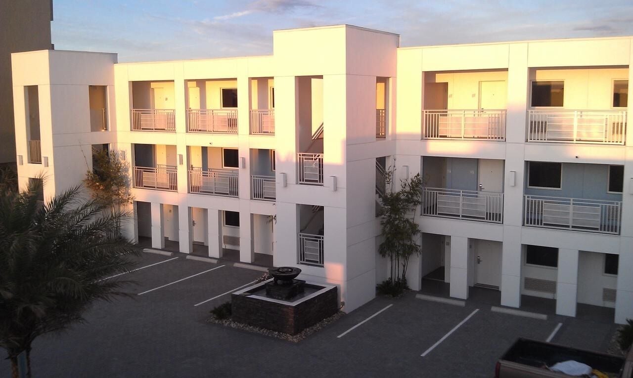 A multi-story hotel with balconies, a courtyard with a fountain, and a parking area.