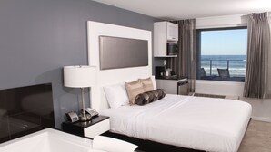 A modern hotel room with a large bed, a separate bathroom, a small kitchenette, and a balcony with a view of the ocean. - Lotus Boutique Inn & Suites (Ormond Beach)