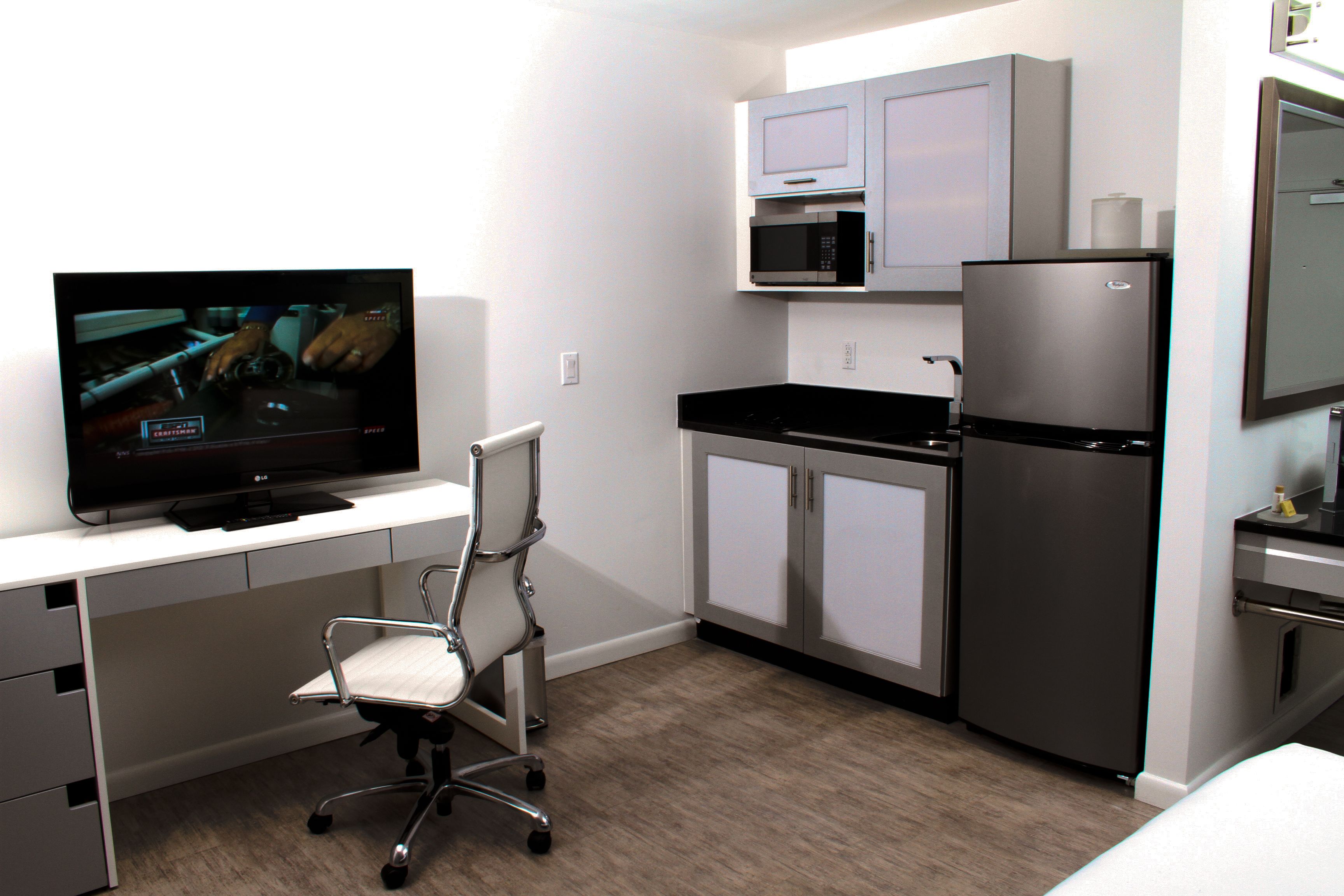 Una cocina moderna con refrigerador, microondas y un televisor sobre un escritorio.