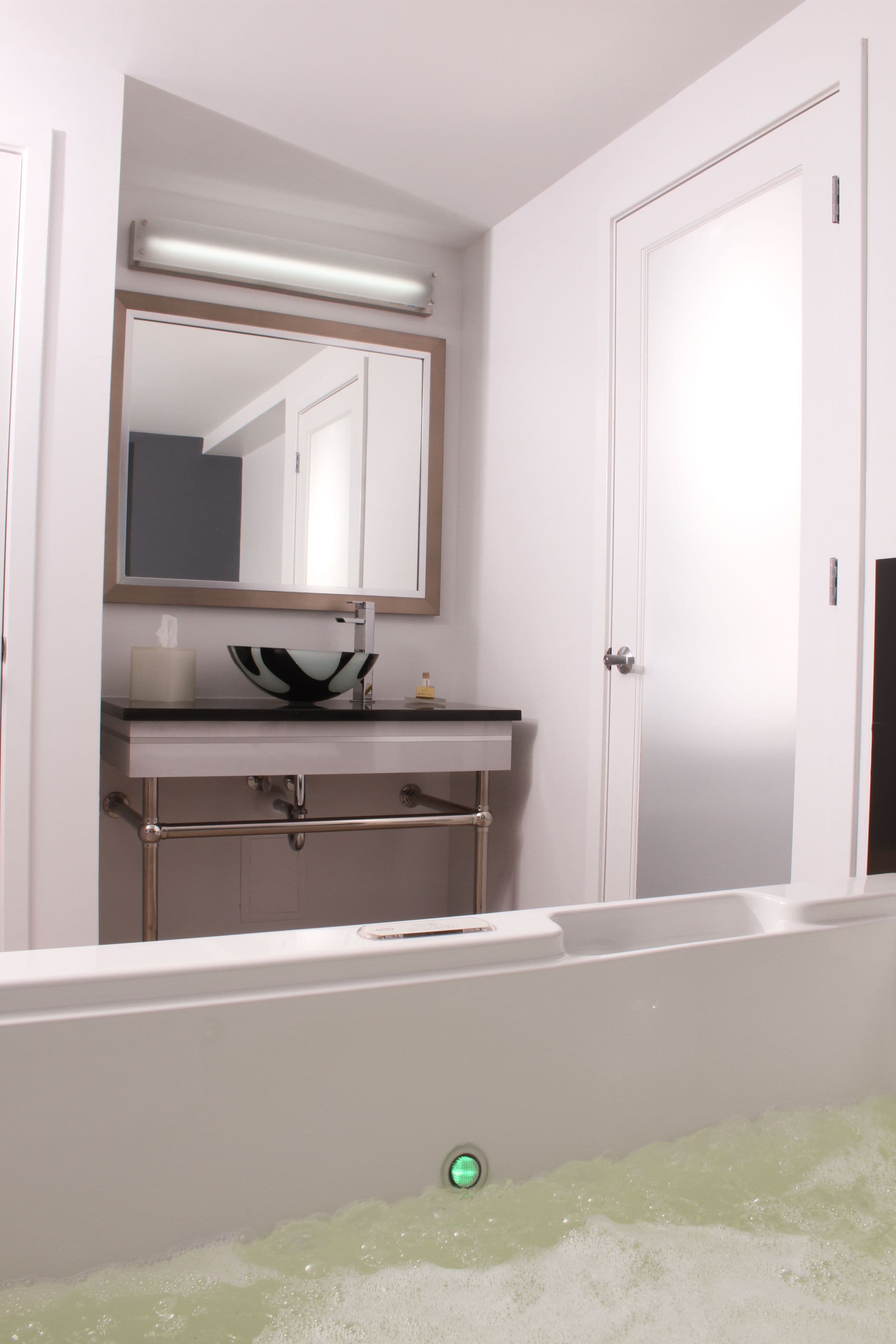 A bathroom with a white sink, a mirror, and a bathtub filled with bubbles.