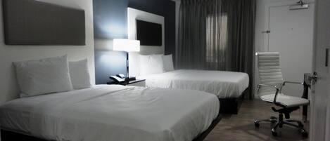 A hotel room with two beds, a desk with a lamp, a chair, and a door.