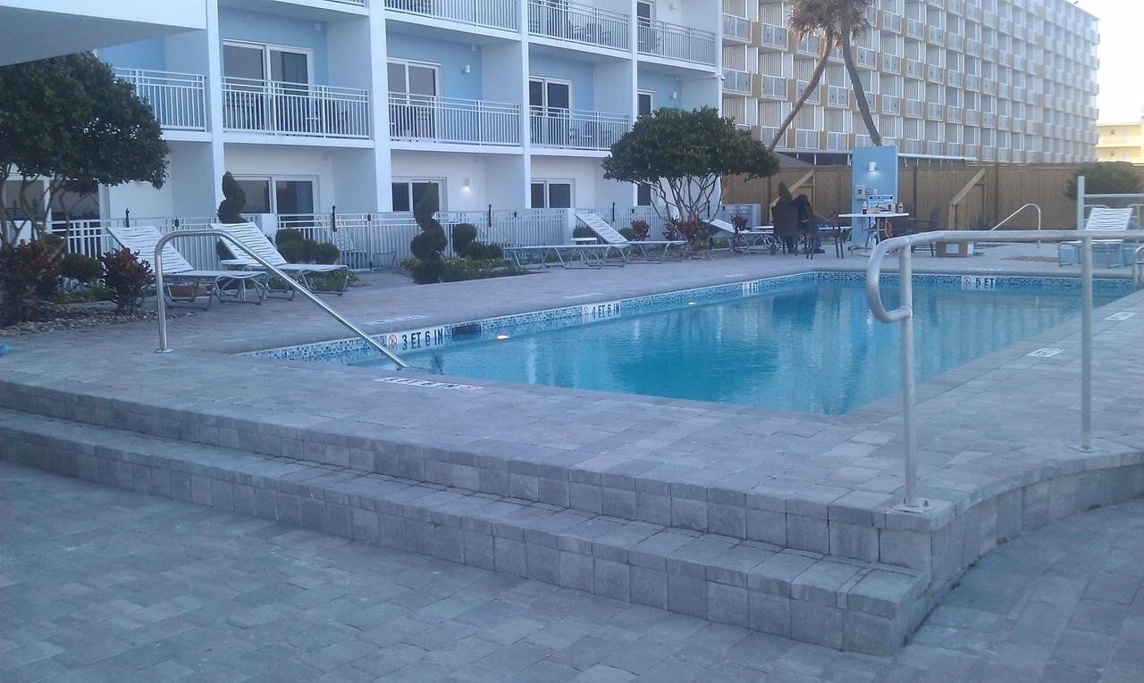 A swimming pool with lounge chairs and a building with balconies in the background.