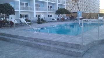 Une piscine avec des chaises longues et, au fond, un bâtiment doté de balcons.