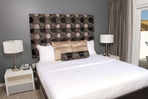 A neatly made bed with white linens and decorative pillows, a bedside lamp, and a small nightstand with a phone and a lamp.