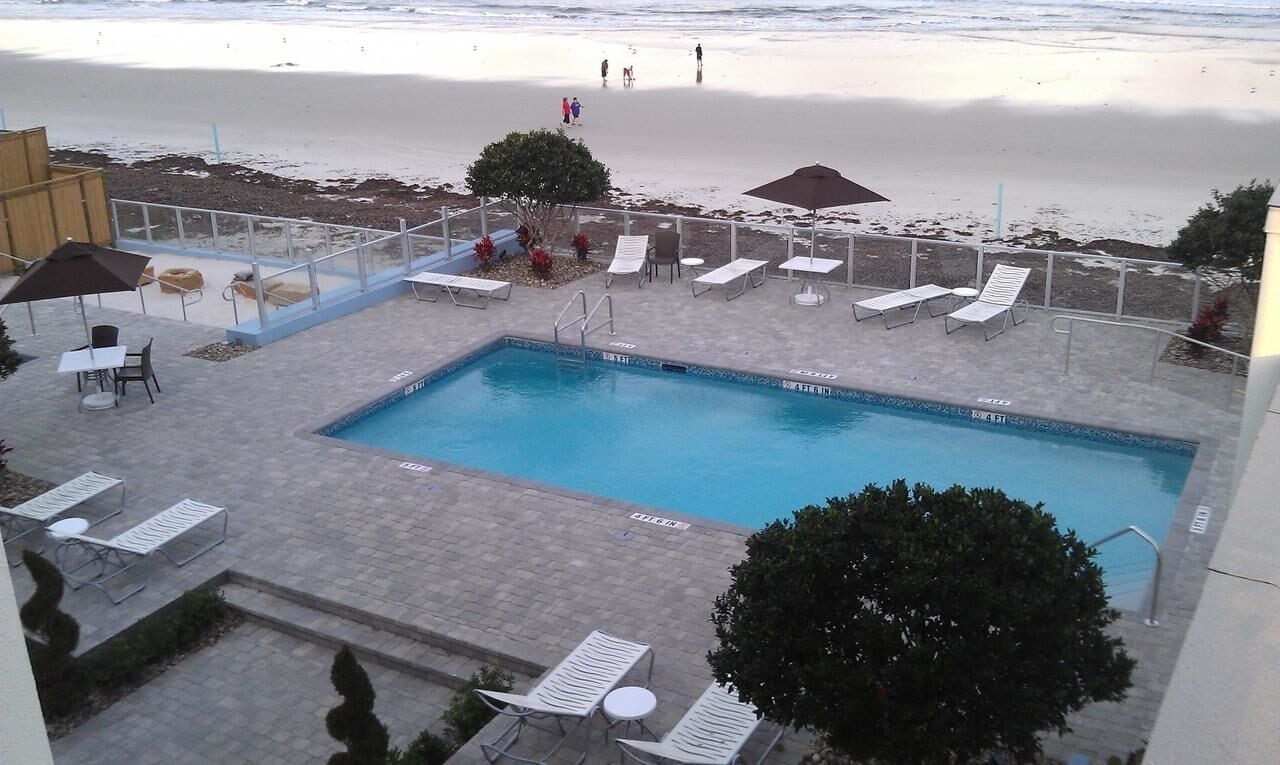 A pool area with lounge chairs and umbrellas, a clear view of the beach, and a lifeguard stand.