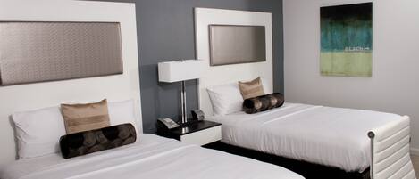 A hotel room with two single beds, a bedside table with a lamp, a phone, and a wall art piece.