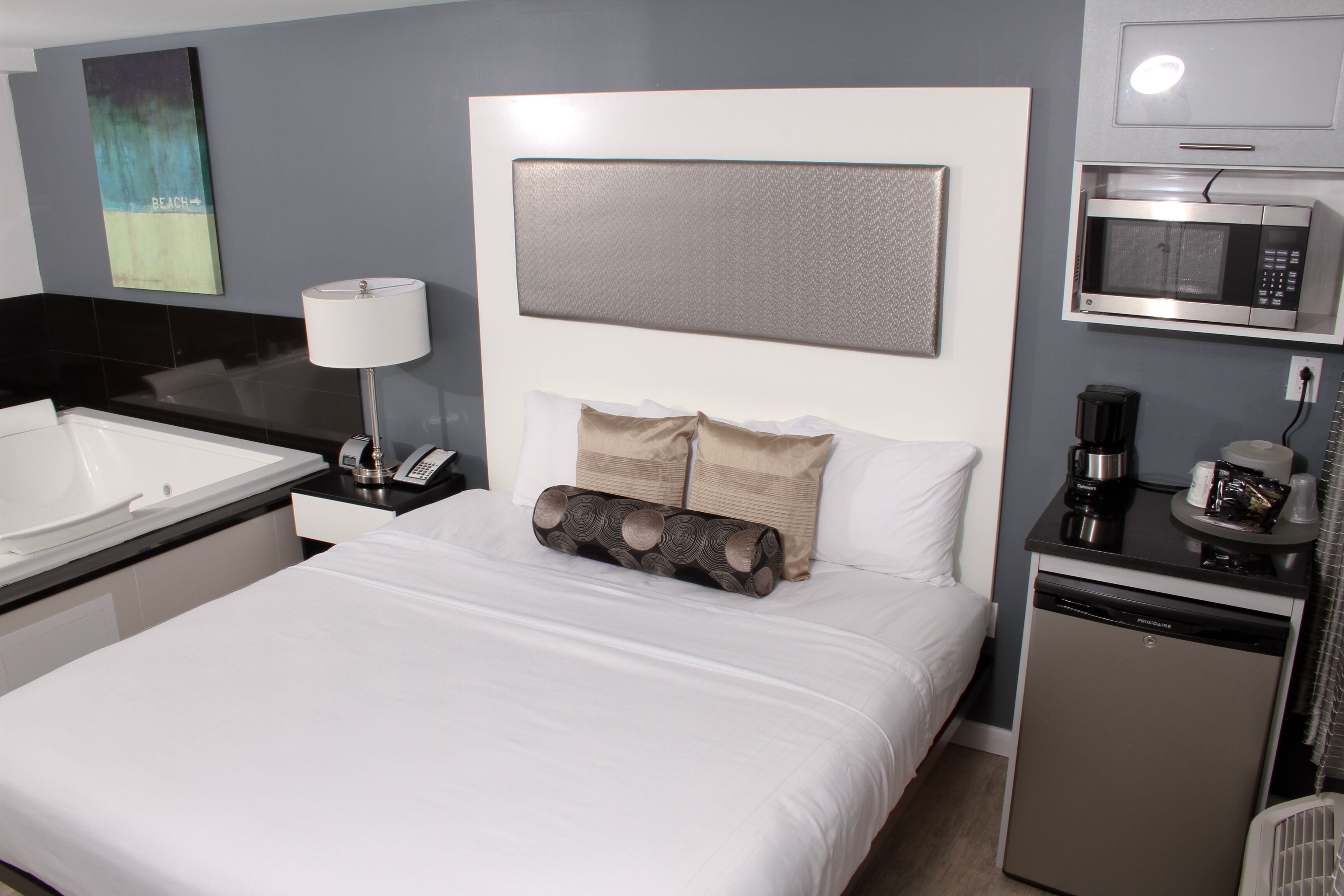A hotel room with a large bed, a separate bathroom with a bathtub, a microwave, a coffee maker, and a small refrigerator.