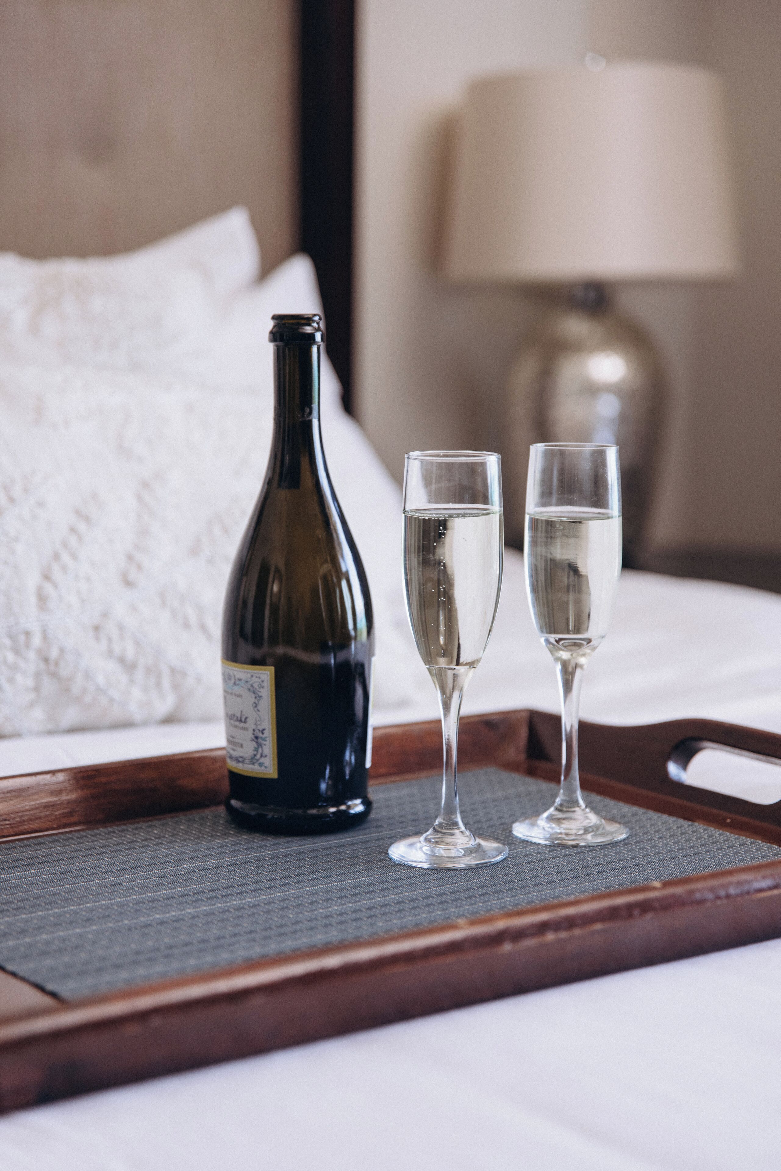 Een fles wijn en twee glaasjes op een dienblad op een bed.