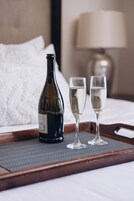 A bottle of wine and two glasses on a tray on a bed.