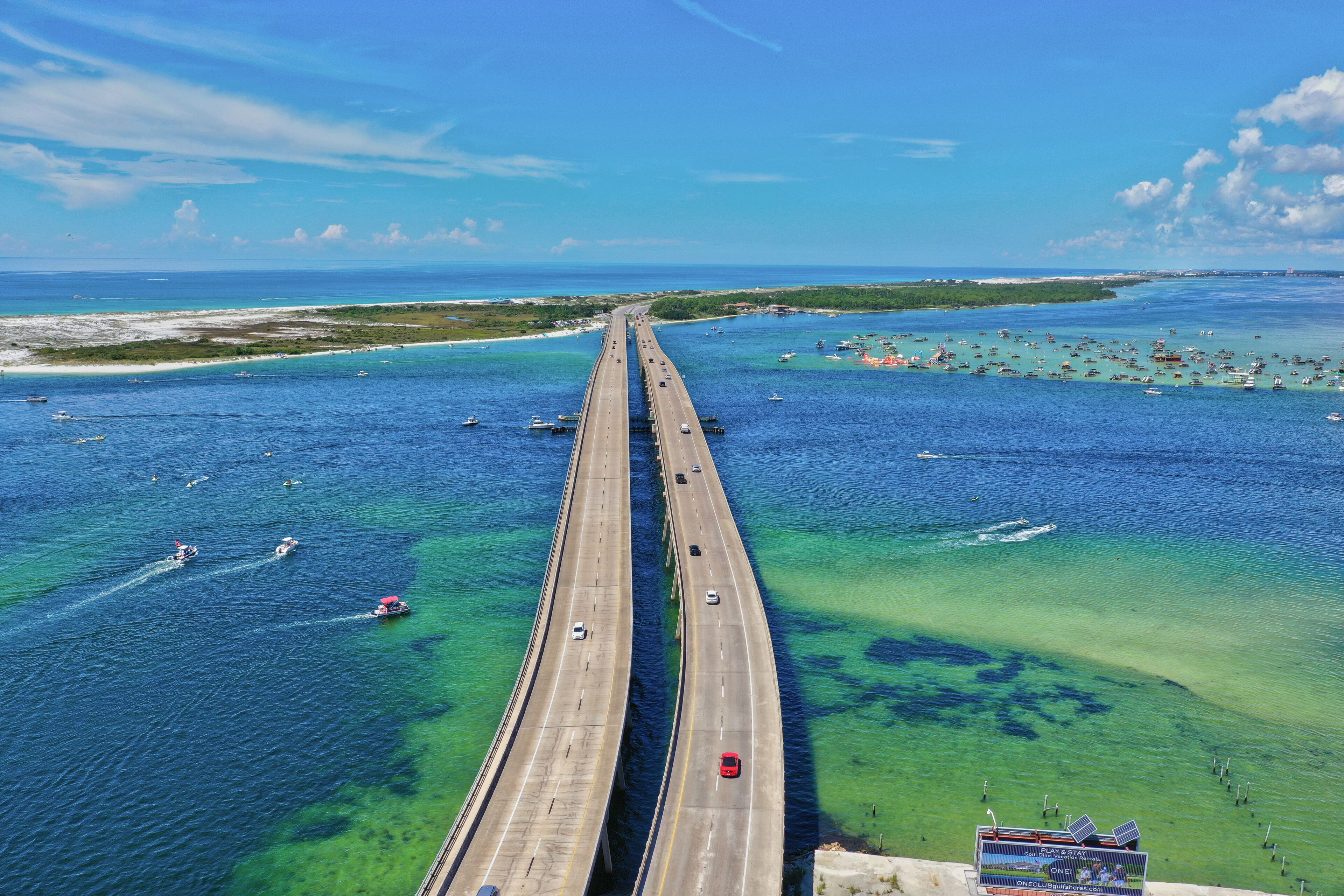 Un largo puente sobre aguas azul cristalino, con barcos y algunos automóviles.