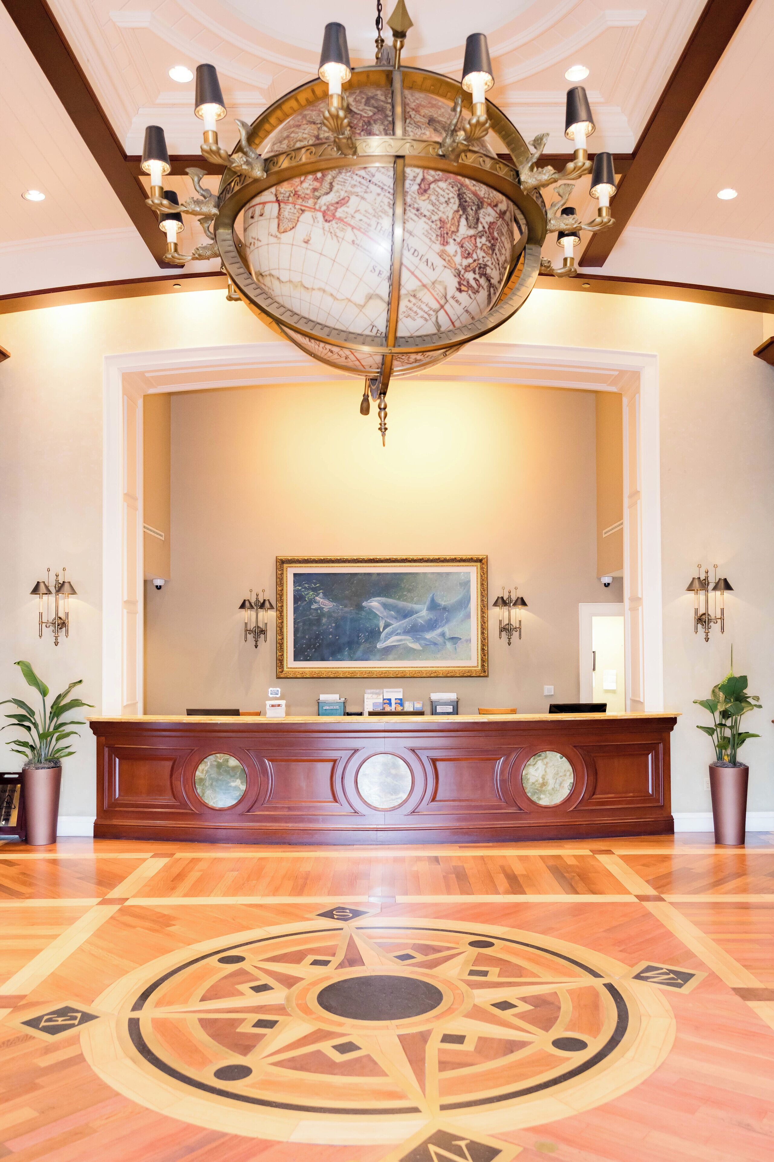 A lobby with a large globe chandelier, a reception desk, and a painting on the wall.