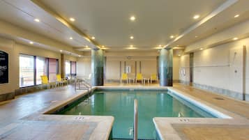 An indoor swimming pool with clear water, tiled walls, and a few yellow chairs around the pool area.