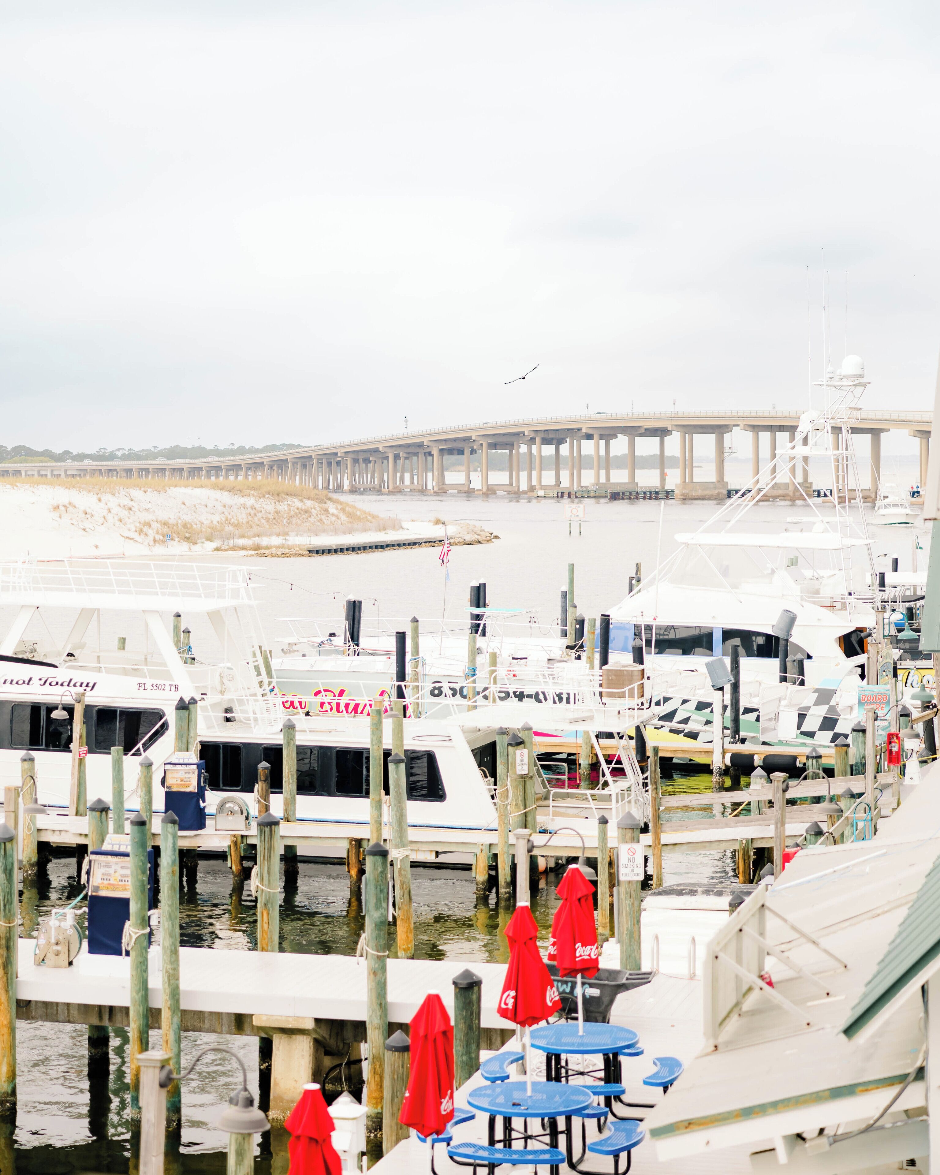 Un puerto deportivo con barcos amarrados, un muelle al fondo y mesas exteriores con sombrillas.