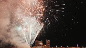 A nighttime view of a waterfront with fireworks display, buildings, and a dock.