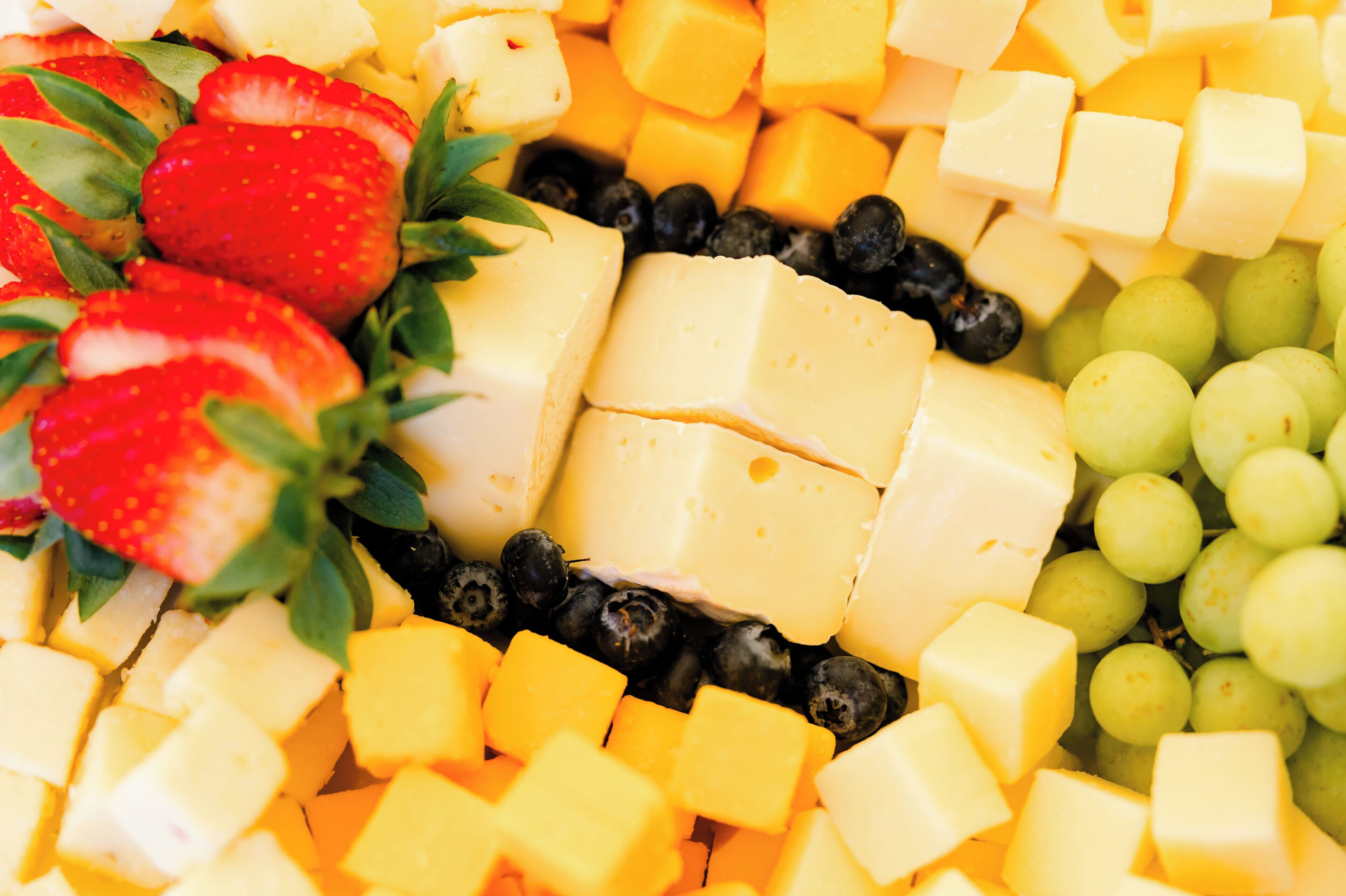 A variety of cheeses, strawberries, blueberries, and grapes.