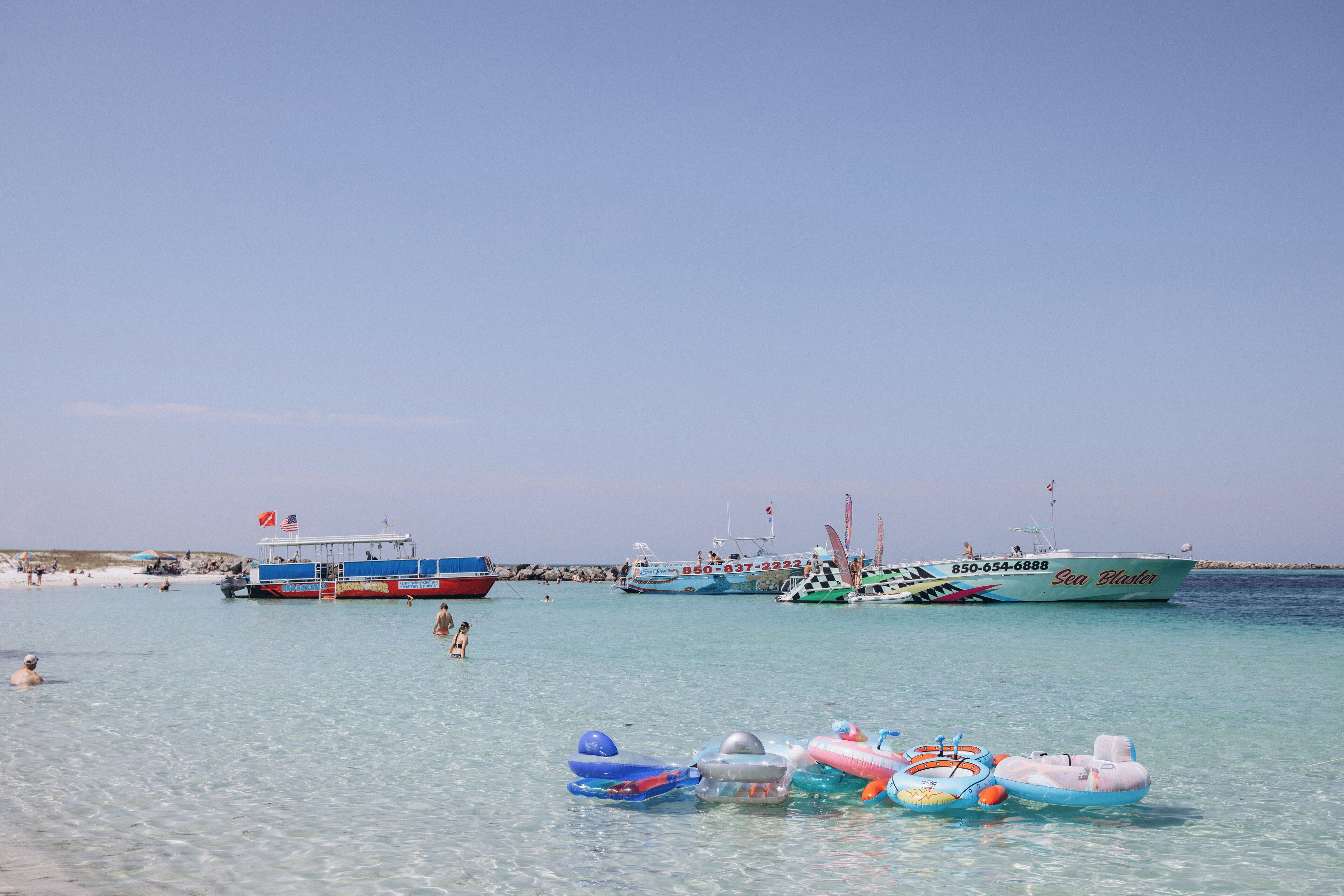Una playa con aguas transparentes, varios barcos y boyas hinchables.