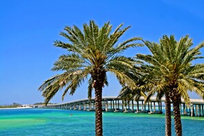 A coastal scene with palm trees and a bridge over turquoise water. - Emerald Grande Condominiums at HarborWalk Village (Destin)