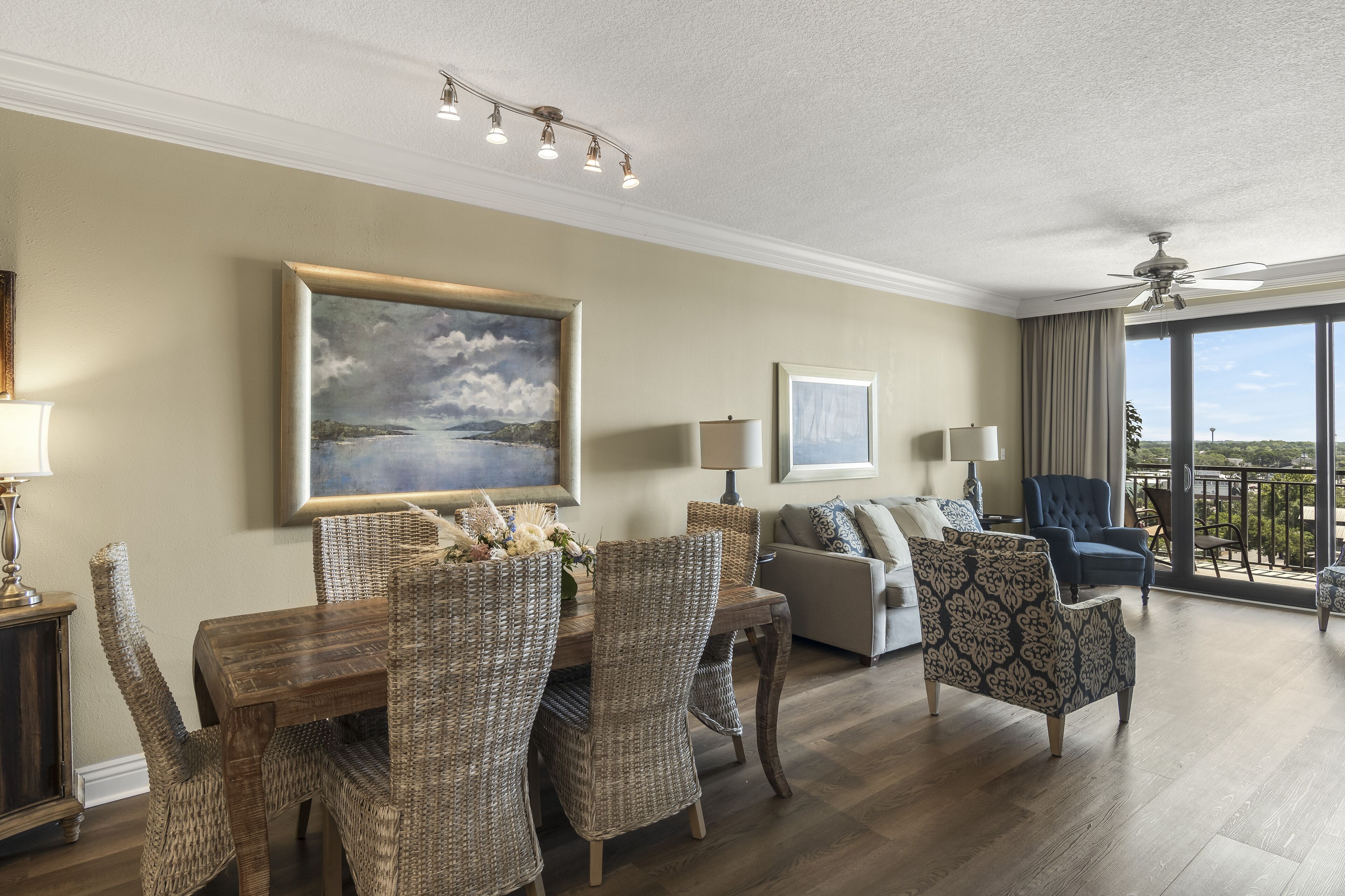 A spacious living room with a dining area, a balcony with a view, and a ceiling fan.
