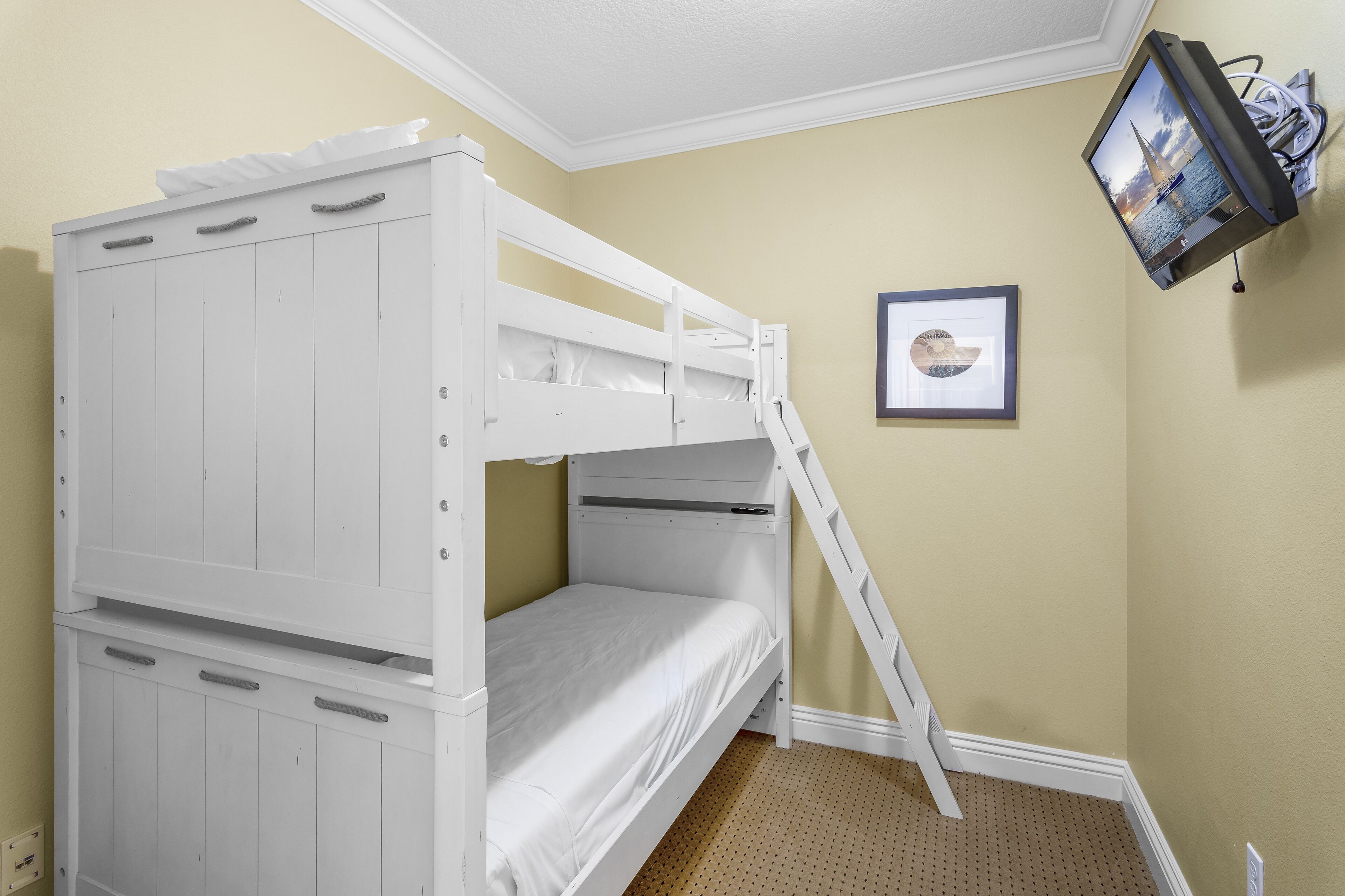 Un lit superposé avec une échelle, un tableau encadré accroché au mur et un téléviseur fixé au mur.