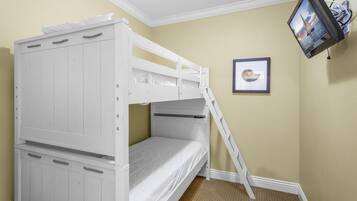 Una cama litera con escalera, un cuadro enmarcado en la pared y un televisor montado en la pared.