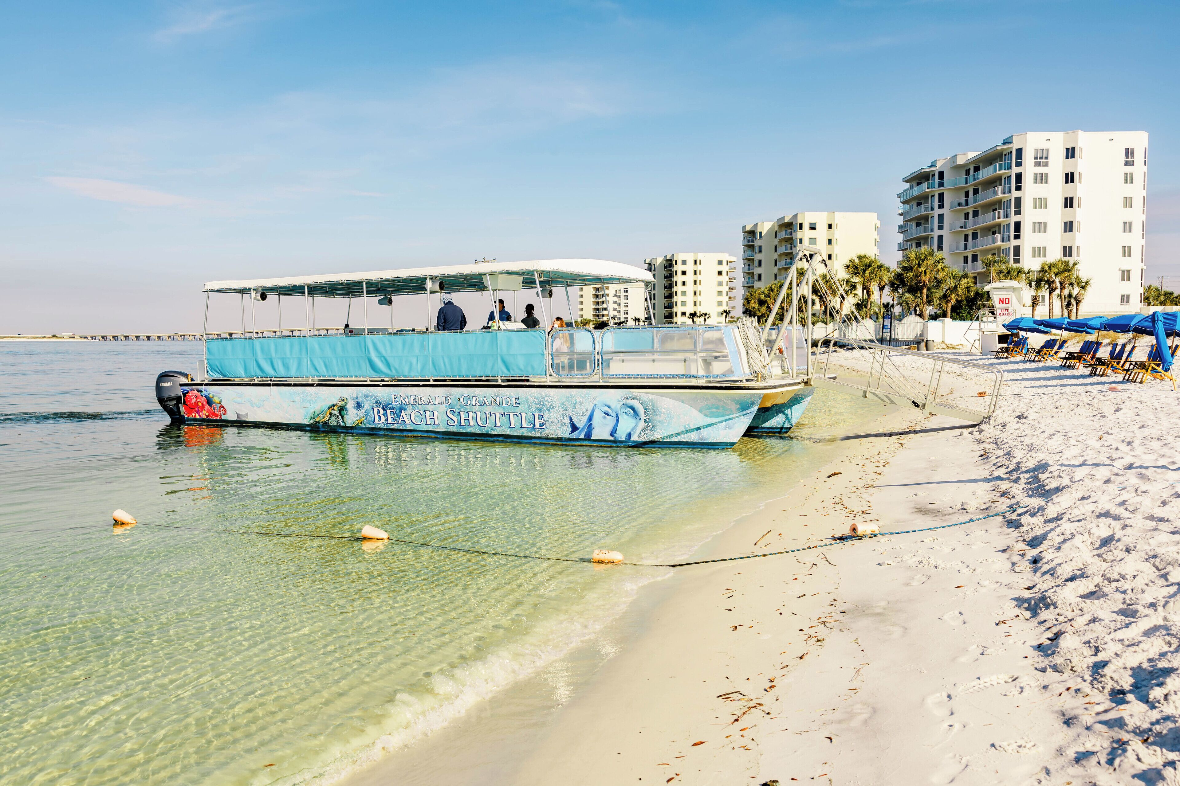 A beach shuttle boat with a blue canopy, a sandy beach, and a row of beach umbrellas.