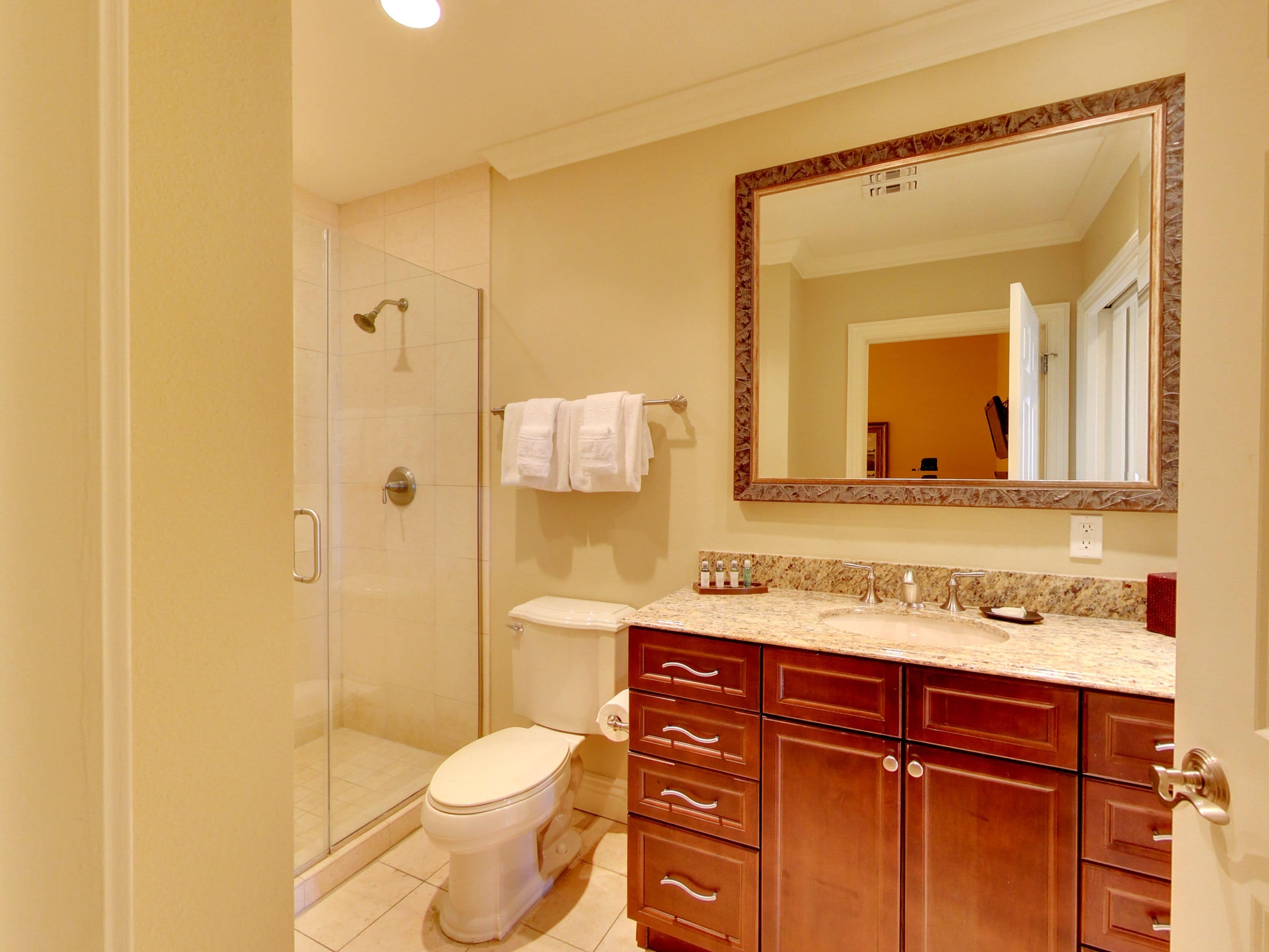 Une salle de bain équipée d’une douche, de toilettes, d’un meuble-lavabo avec des tiroirs et d’un grand miroir.