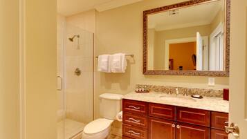 A bathroom with a shower, toilet, vanity with drawers, and a large mirror.
