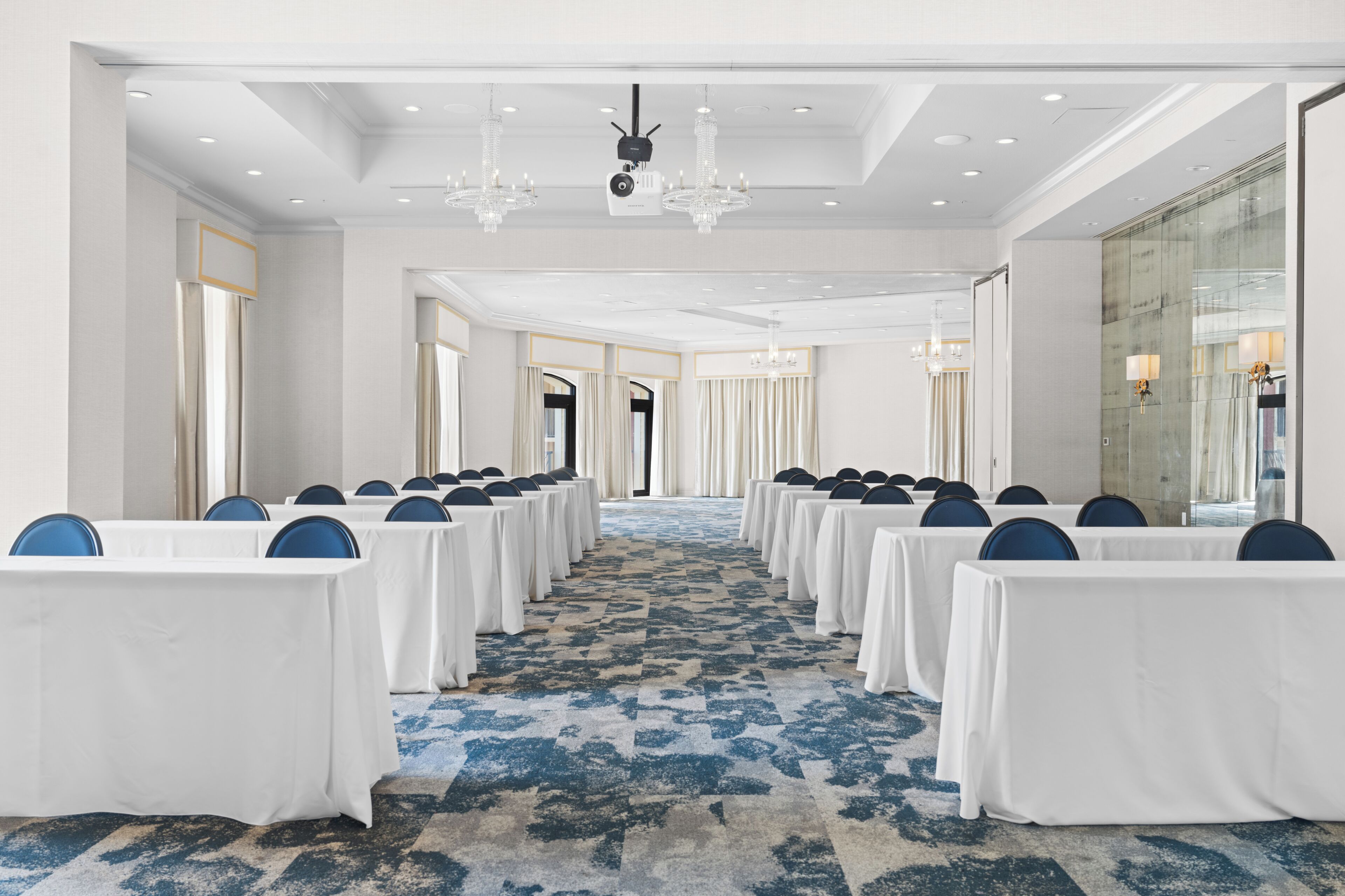A conference room with rows of tables and chairs, a patterned carpet, and chandeliers.