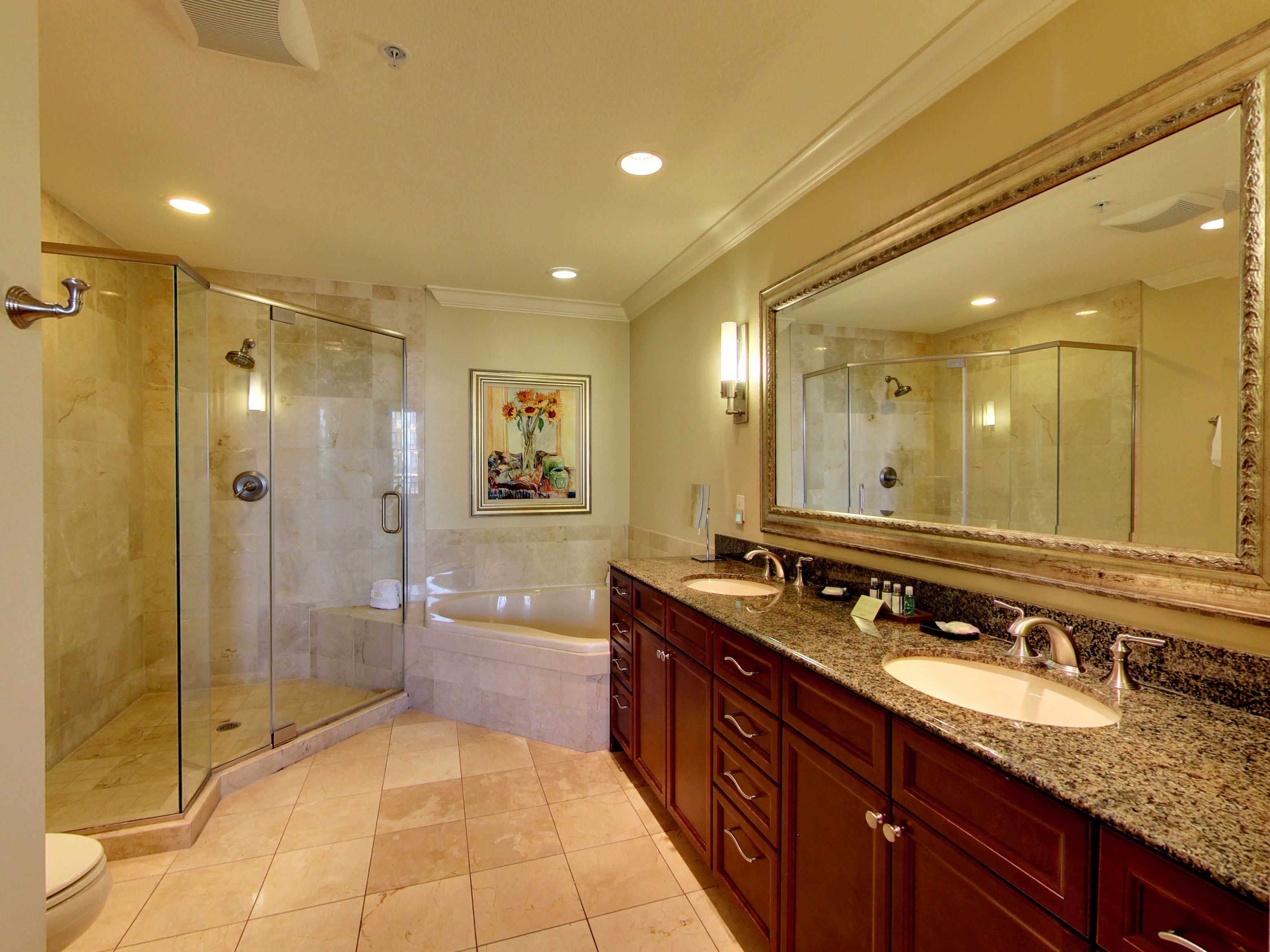 A spacious bathroom with a glass-enclosed shower, a large bathtub, and two sinks.