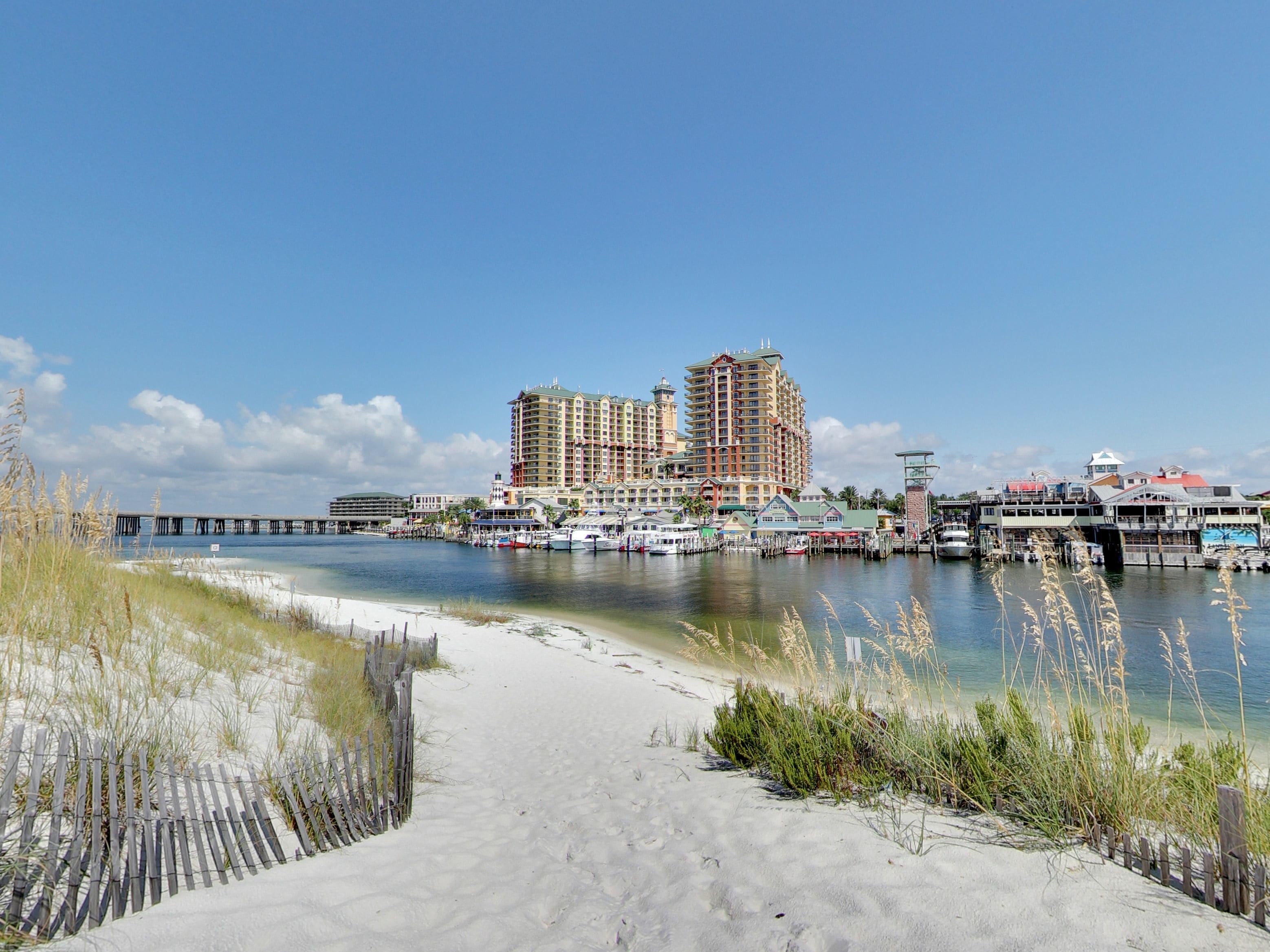 A coastal cityscape with a sandy beach, a pier, and a marina with boats.