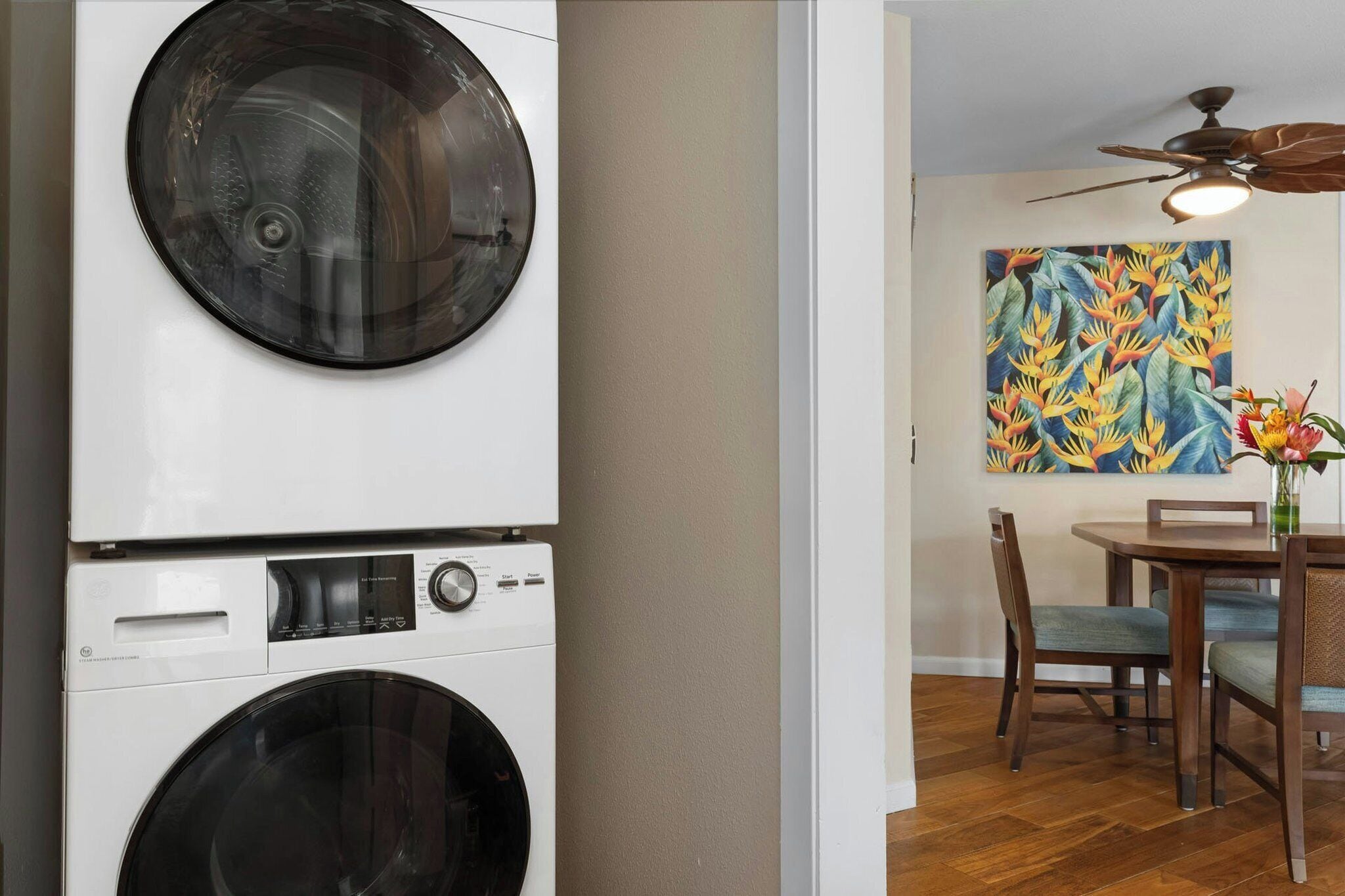 Una sala de lavandería con lavadoras apiladas y un comedor con una mesa, sillas y un ventilador de techo.