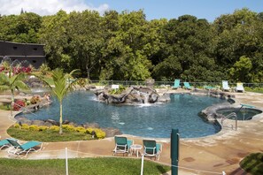 Un espace piscine agrémenté de plusieurs éléments aquatiques, dont une cascade, entouré de chaises longues et d’un mur en pierre.