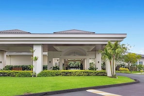 Un hotel moderno con entrada cubierta, césped cuidado y palmeras.