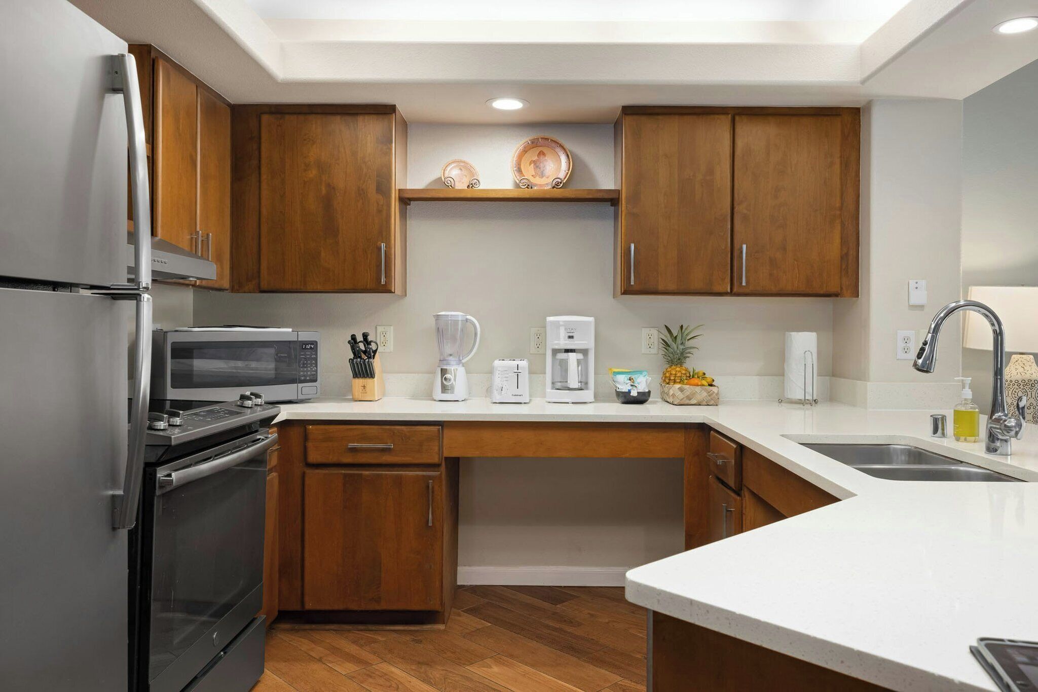 A modern kitchen with wooden cabinets, a stainless steel refrigerator, a microwave, a coffee maker, and a sink.