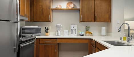 A modern kitchen with wooden cabinets, a stainless steel refrigerator, a microwave, a coffee maker, and a sink.