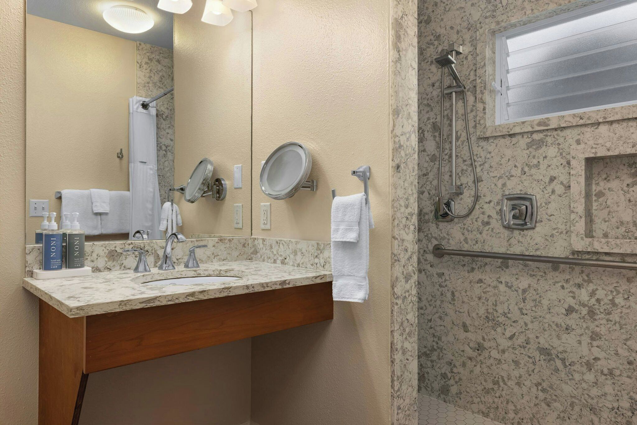 A bathroom with a marble sink, two mirrors, a towel rack, and a shower area.