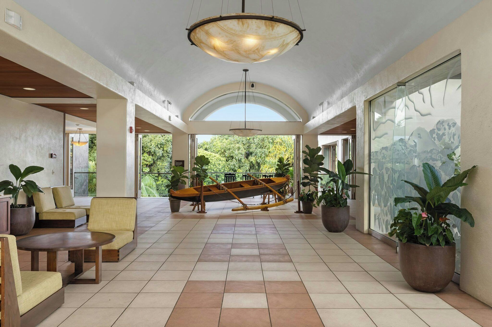 A spacious lobby with a high ceiling, a central seating area with a swing chair, and potted plants.